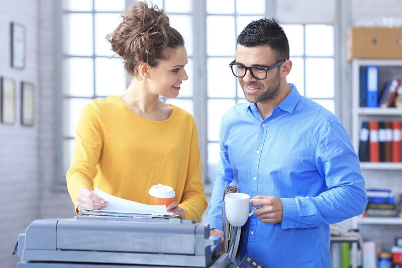 Man and woman at printer discussing over paper with coffee